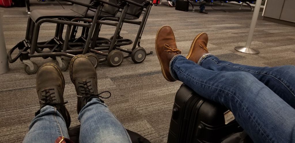 Two pairs of legs are propped up on their luggage at an airport